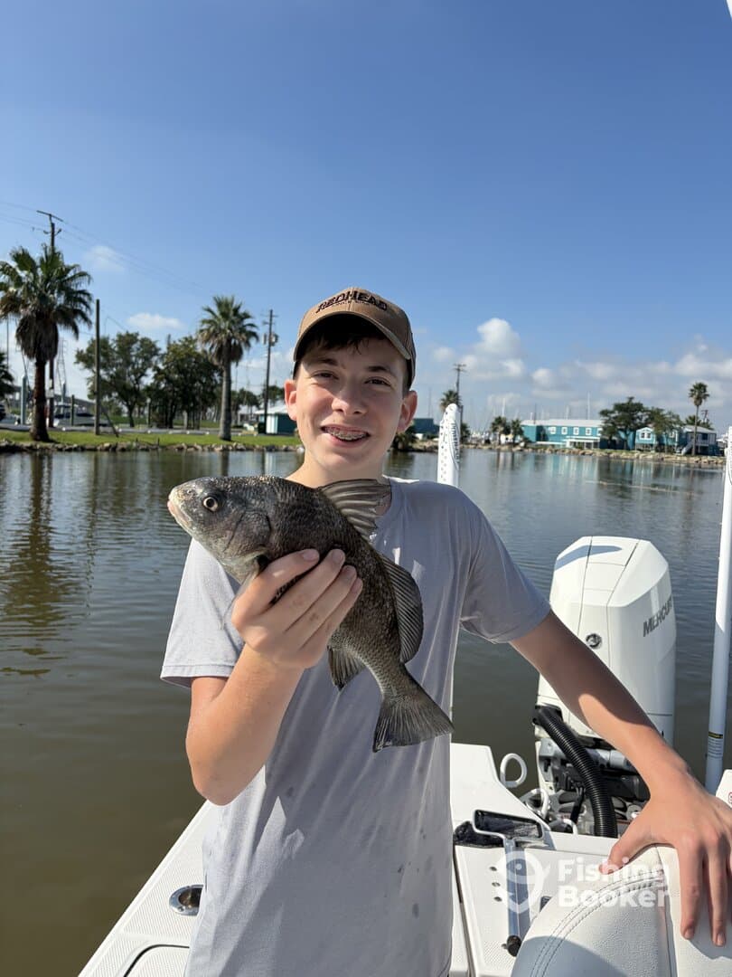 A young angler proudly holding a Black Drum while fishing from a boat in a scenic waterway.