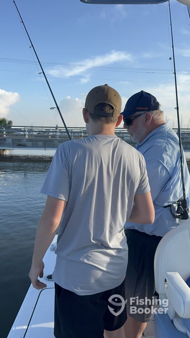 A young angler and an experienced fisherman are engaged in fishing on a boat, showcasing a moment of learning and excitement.