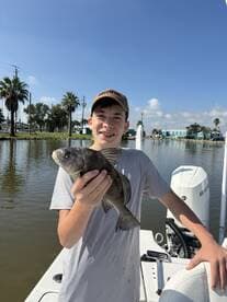 A young angler proudly holding a Black Drum while fishing from a boat in a scenic waterway.