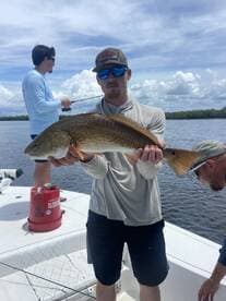 Angler proudly displaying a large Redfish while fishing on a boat in a scenic coastal environment.