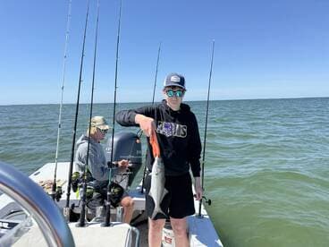 A young angler proudly displaying a fish while fishing on a boat, with another person engaged in fishing activities in the background.