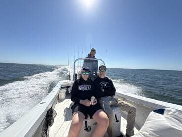 Three anglers enjoying a day on a center console boat, cruising through calm waters under a clear blue sky.