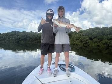 Two young anglers proudly displaying a Redfish while fishing in a serene mangrove environment.