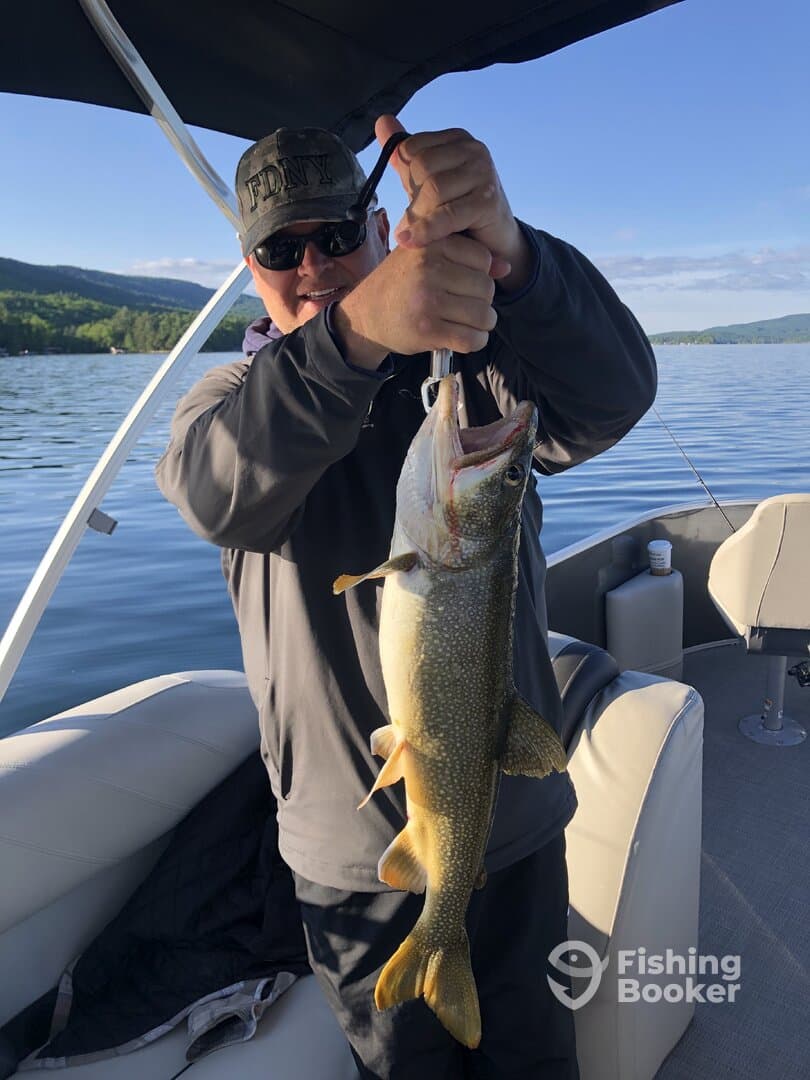 Angler proudly displaying a large Lake Trout while fishing on a serene lake, showcasing the excitement of a successful catch.