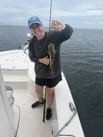 A happy angler holding a freshly caught fish while fishing from a boat in calm waters.