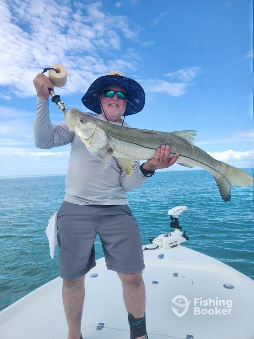 Angler proudly displaying a large Snook while fishing on a boat in clear blue waters.