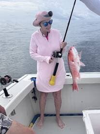 A smiling angler proudly displays a freshly caught Red Snapper while fishing on a boat, showcasing a serene ocean backdrop.