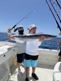 Two anglers proudly displaying a large King Mackerel aboard a fishing boat, showcasing a successful day on the water.