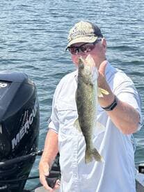 An angler proudly displaying a Walleye while fishing on a sunny day, with a Mercury outboard motor visible in the background.