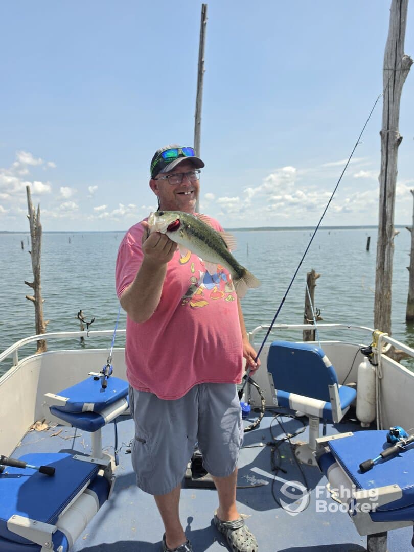 Angler proudly displaying a large Largemouth Bass while fishing on a boat in a serene lake setting.