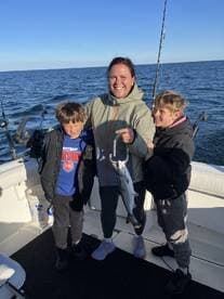 A family enjoying a fishing trip, with a proud moment as a mother holds a freshly caught fish while her two sons stand beside her on the boat.