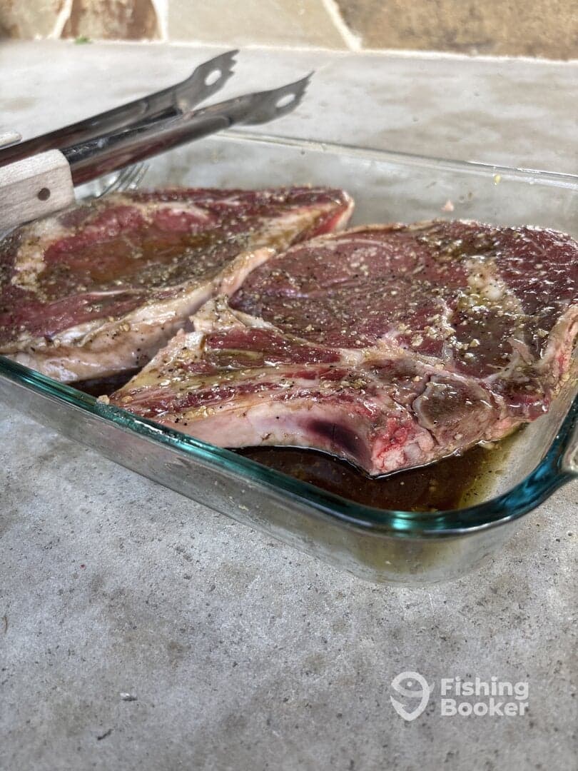 Image shows marinated steaks in a glass dish, with tongs resting beside them, but does not relate to fishing or catch.