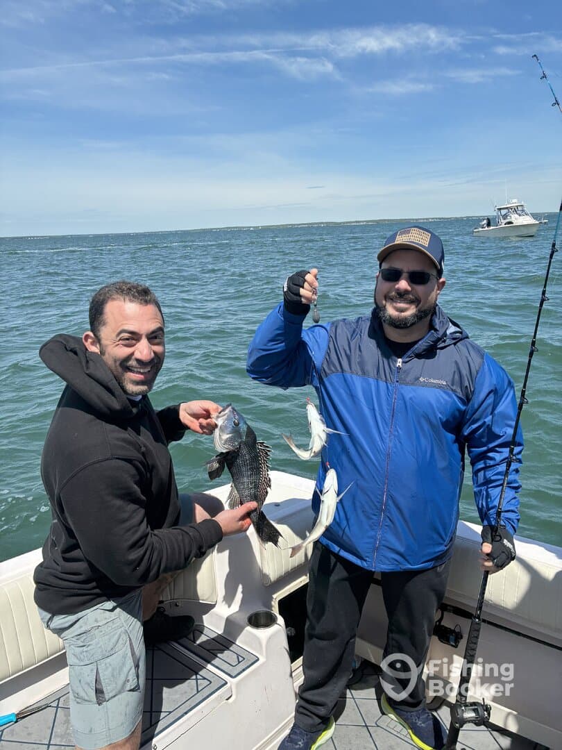 Two anglers proudly displaying their catch, including a large Black Sea Bass, while fishing on a boat in open waters.