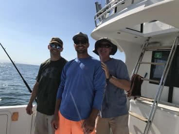 Three anglers enjoying a sunny day on a fishing charter, posing on the boat's deck with the ocean in the background.