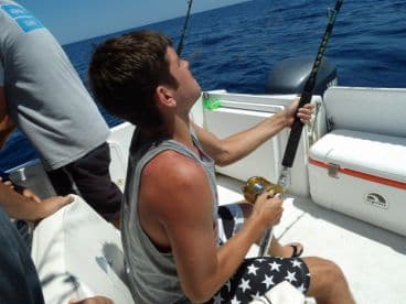 A young angler is actively reeling in a catch while fishing on a boat in open waters, showcasing the excitement of deep-sea fishing.