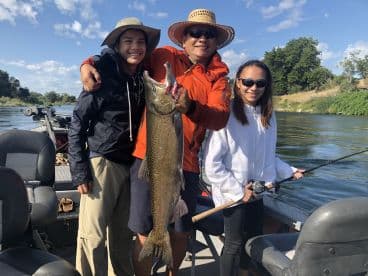 A family enjoying a successful fishing trip, proudly displaying a large trout caught on a river, with a scenic backdrop.