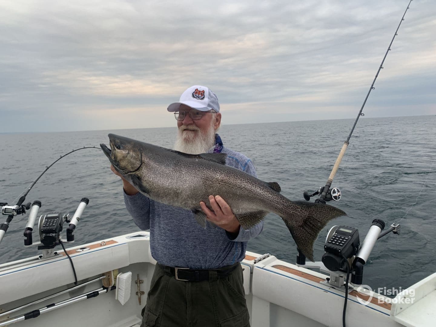 An angler proudly displaying a large Lake Trout while fishing on a boat in open water.