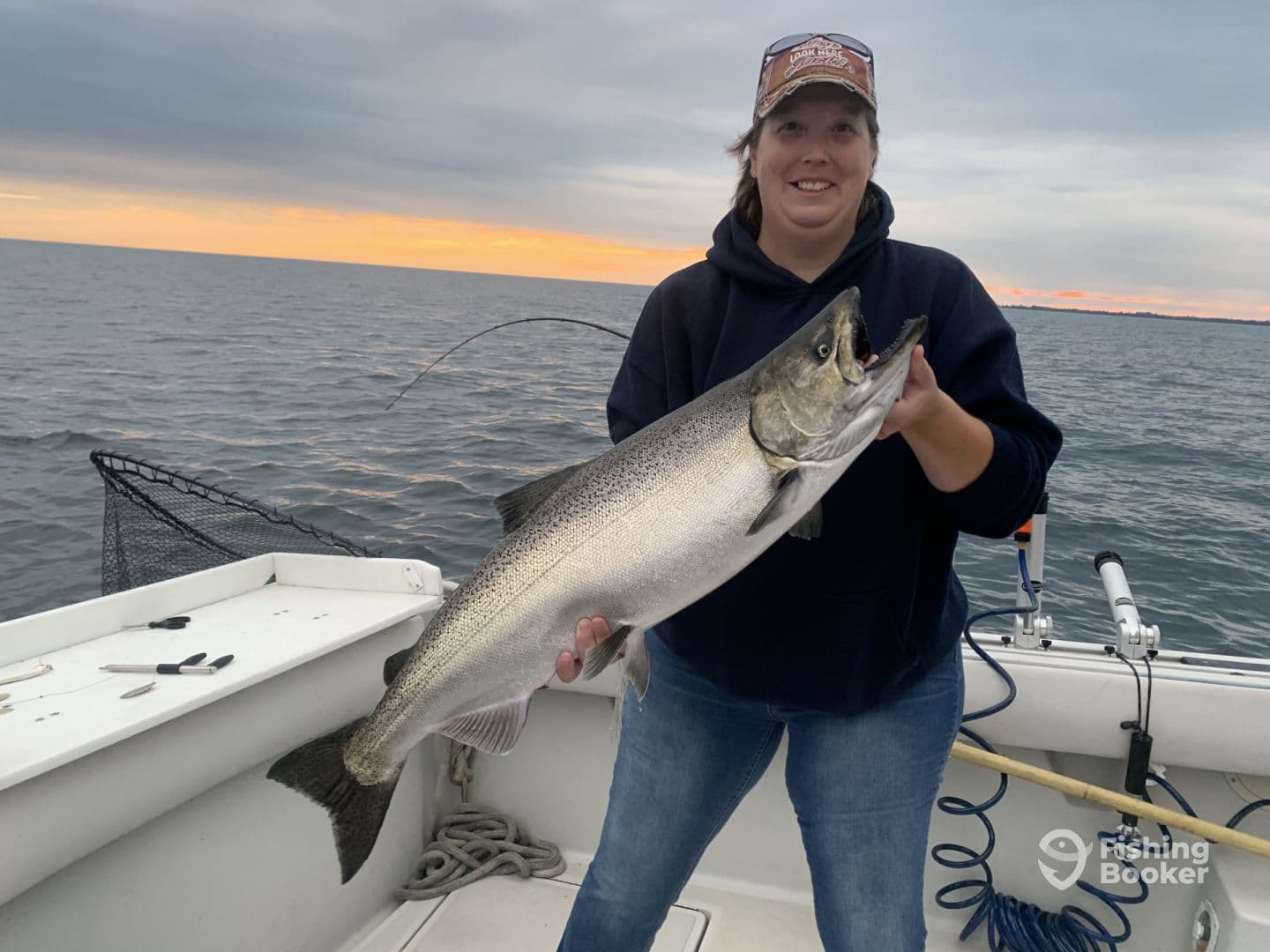 Angler proudly displaying a large Salmon while fishing on a boat during sunset.