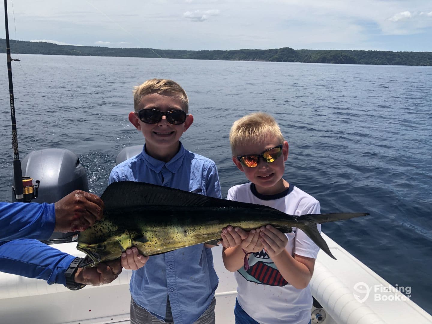 Two young anglers proudly displaying a Mahi Mahi while fishing on a boat in clear blue waters.