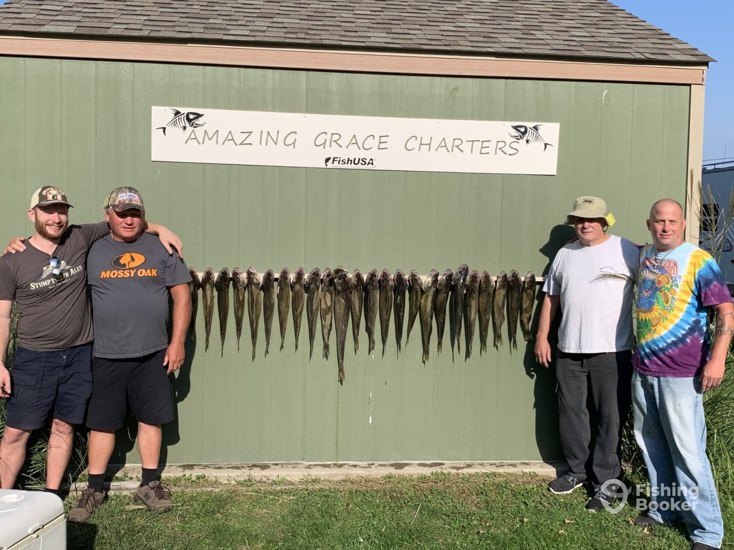 Group of four anglers proudly posing in front of a display of freshly caught fish after a successful charter trip with Amazing Grace Charters.