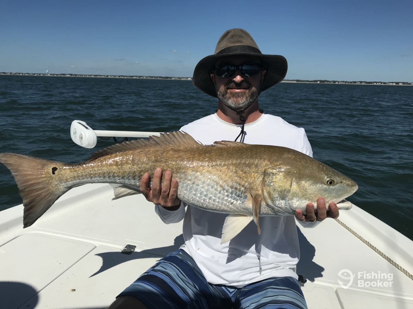 An angler proudly displaying a large Redfish while on a boat in a coastal fishing environment.