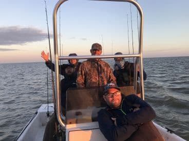 Group of anglers enjoying a fishing trip on a boat, with rods ready for action against a scenic sunset backdrop.