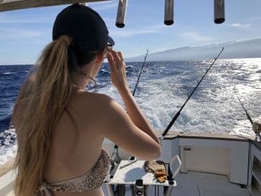 A young angler on a sport fishing boat, focused on the ocean while preparing for a catch in a vibrant blue sea.