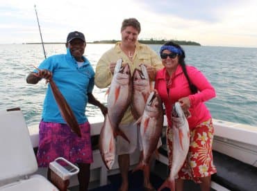 Three anglers proudly displaying their catch of Red Snapper aboard a fishing boat, showcasing a successful day on the water.