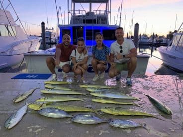 A group of three adults proudly displaying a catch of Mahi Mahi on the dock after a successful fishing trip.