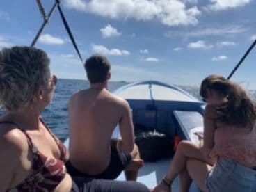 A group of three individuals enjoying a sunny day on a fishing boat, with a clear view of the ocean and blue skies.