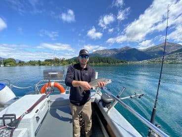 Angler holding a Rainbow Trout while fishing on a scenic lake surrounded by mountains.
