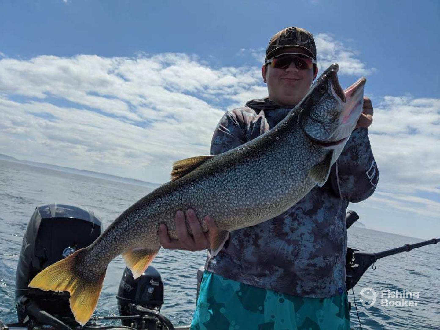 A young angler proudly displaying a large Lake Trout while fishing on a boat in open waters.