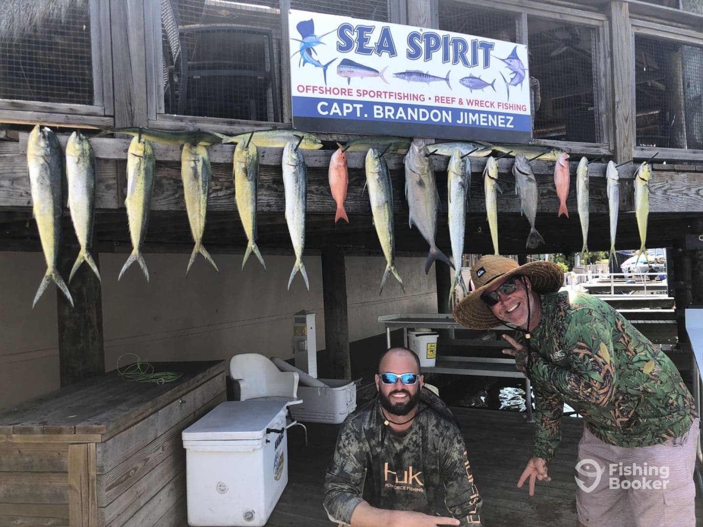 Two anglers posing in front of a catch board displaying several Mahi Mahi and a Red Snapper, showcasing a successful offshore fishing trip.