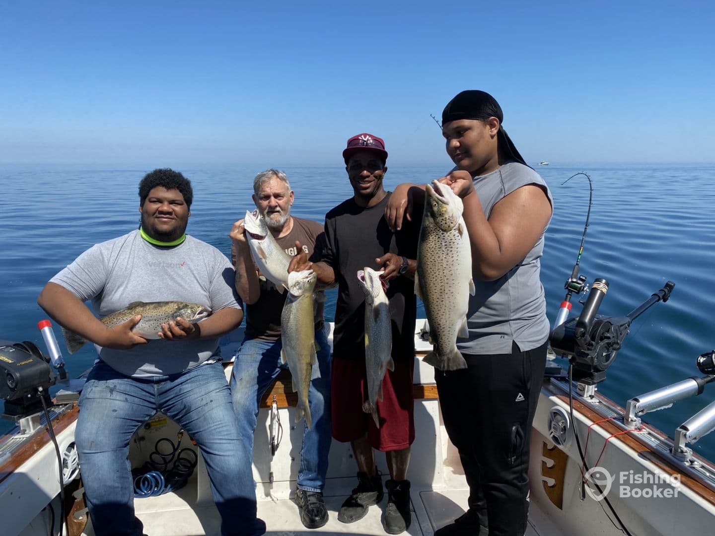 A group of anglers proudly displaying their catch of trout and other fish aboard a fishing boat on a clear day.