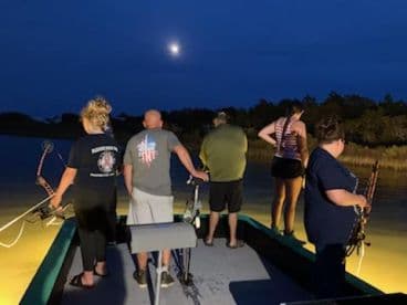A group of anglers preparing to fish at night on a boat, illuminated by the moonlight, showcasing a unique fishing experience.