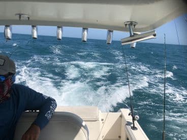 Interior view of a fishing boat showing the helm and seating area, with a fisherman relaxing as the boat navigates through the ocean waves.