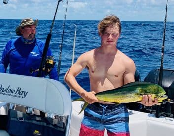 A young angler proudly displaying a vibrant Mahi-Mahi while fishing offshore, with a fellow angler in the background.