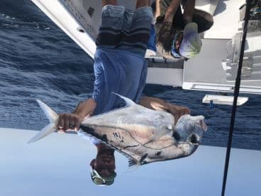 An angler proudly displaying a large Permit caught during a deep-sea fishing trip.