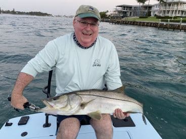 An angler proudly displaying a large Snook while fishing from a boat in a coastal waterway.