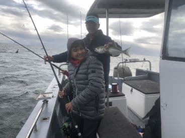 A young angler joyfully holds up a caught fish while fishing with an adult on a boat, showcasing a fun family fishing experience.