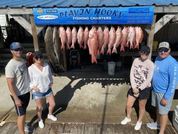 A group of anglers proudly posing in front of a catch board displaying an impressive haul of Red Snapper and Ling after a successful fishing trip with Playin' Hooky Fishing Charters.