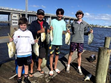 A group of young anglers proudly displaying their catch of Yellowtail Snapper at the dock, showcasing a successful fishing trip.