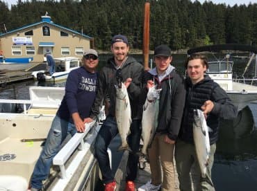 Group of anglers proudly displaying their catch of Salmon at the dock, showcasing a successful fishing trip.