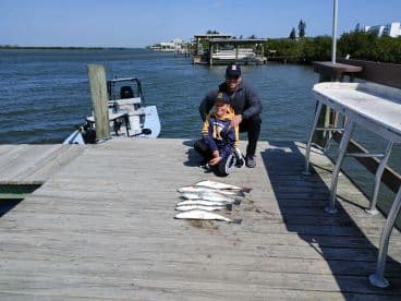 A proud father and son duo display their catch of several Speckled Trout on the dock after a successful fishing trip.