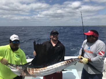 Three anglers proudly displaying a large Sailfish aboard a sportfishing boat, showcasing a successful deep-sea fishing trip.