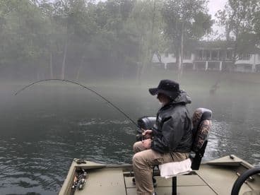 An angler reeling in a catch on a foggy morning, showcasing a serene fishing environment on a calm lake.