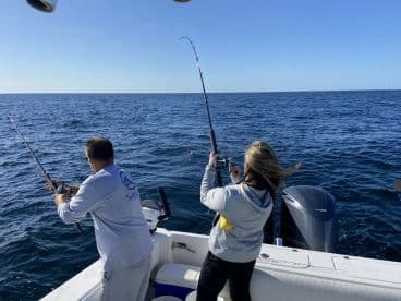 Two anglers actively reeling in their lines while fishing on a sunny day in open waters, showcasing the excitement of the catch.