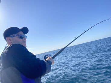 Angler engaged in fishing, reeling in a catch on a clear day at sea.
