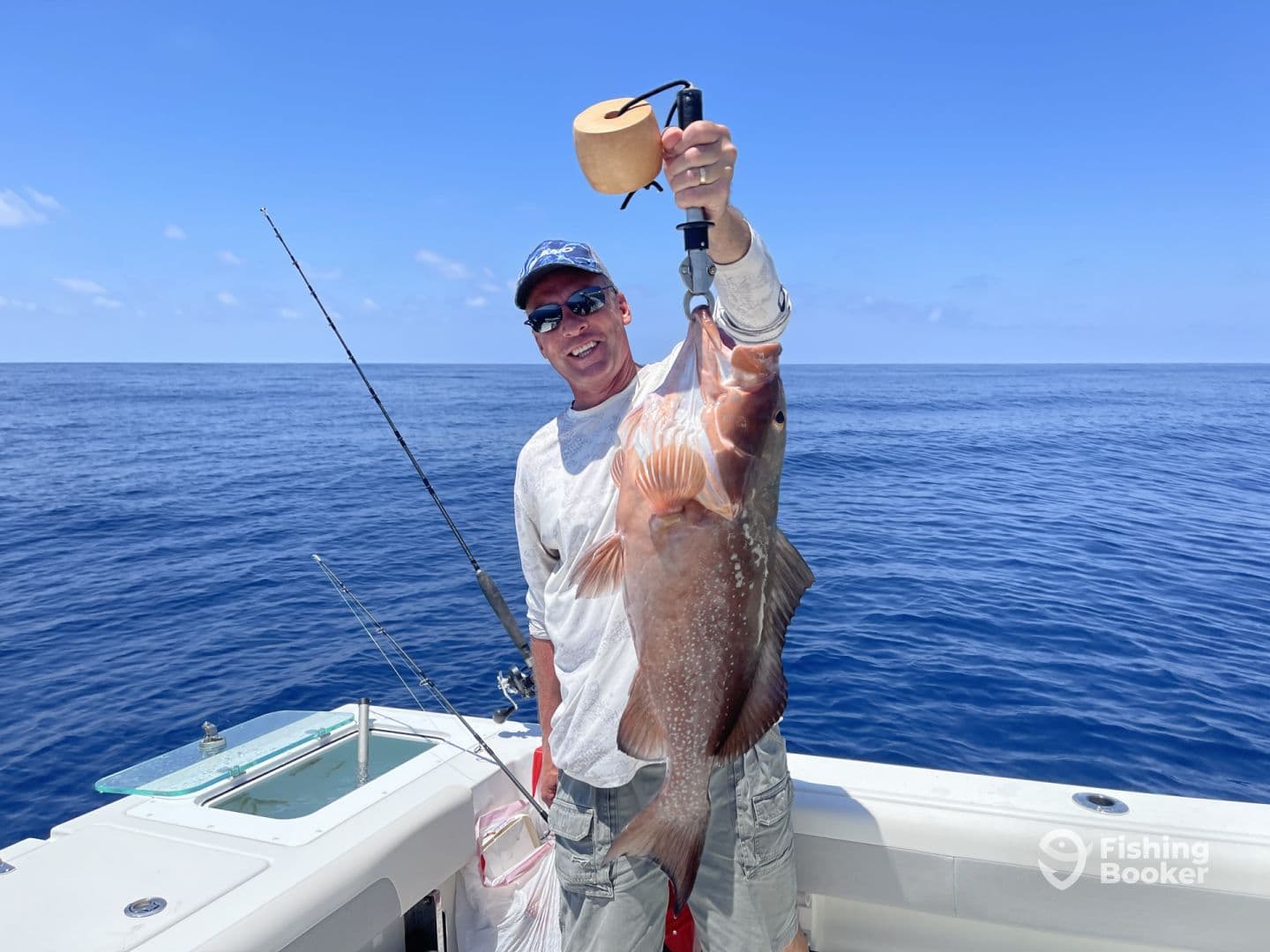 An angler proudly displaying a large Red Grouper while fishing offshore, showcasing a clear blue sky and calm ocean waters.