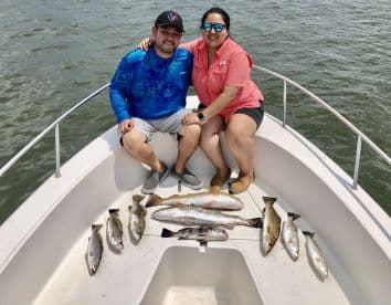 A couple enjoying their fishing trip on a boat, showcasing a variety of Speckled Trout laid out on the deck.